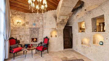 A stone-walled room with a fireplace, two red upholstered chairs, a chandelier, and a wooden ceiling.
