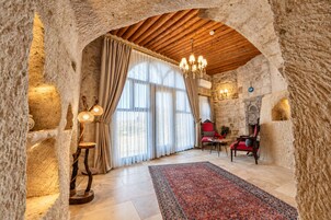 Una habitación con paredes de piedra, techo de madera, un candelabro, chimenea y un sofá rojo.