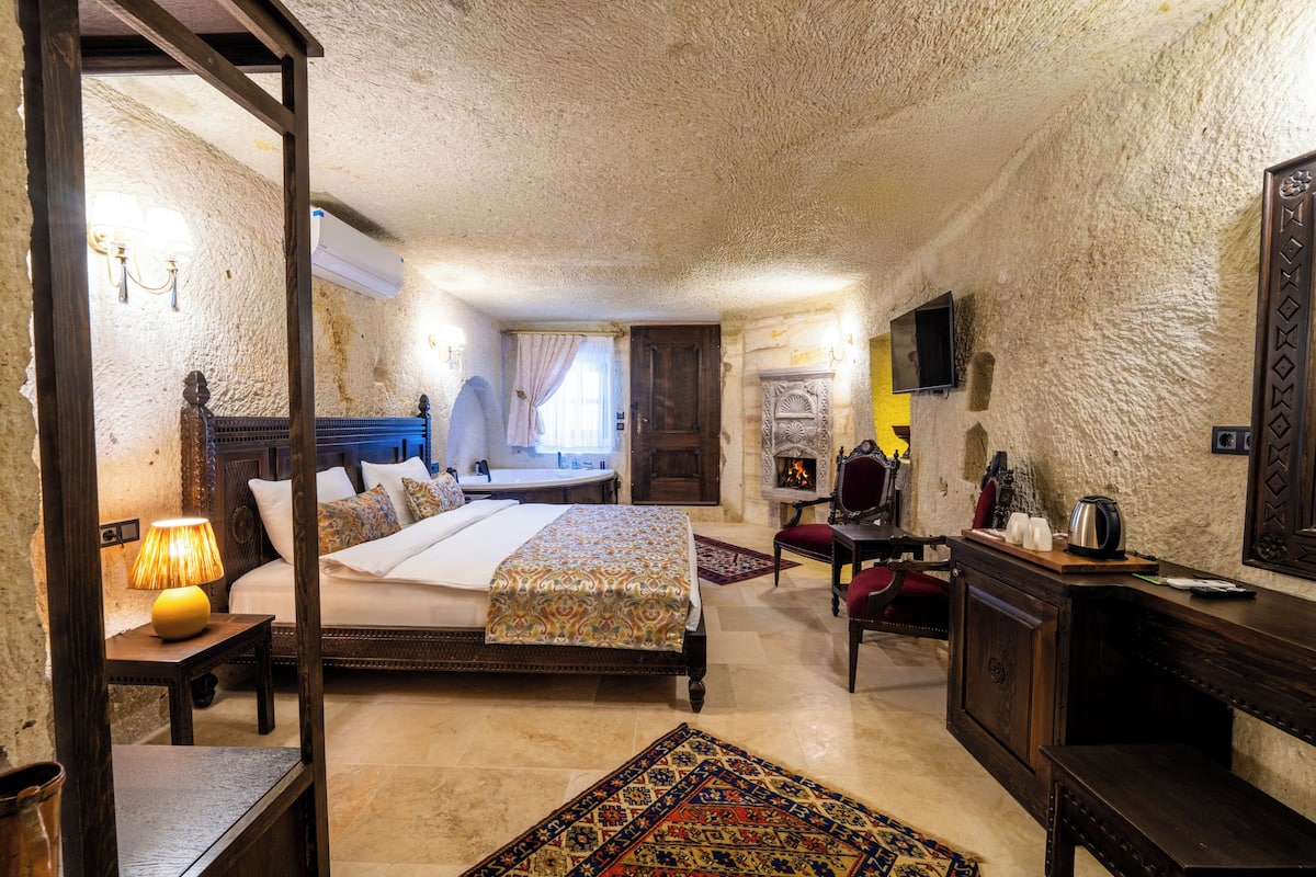 Um quarto com cama, mesa de cabeceira, abajur e lareira.