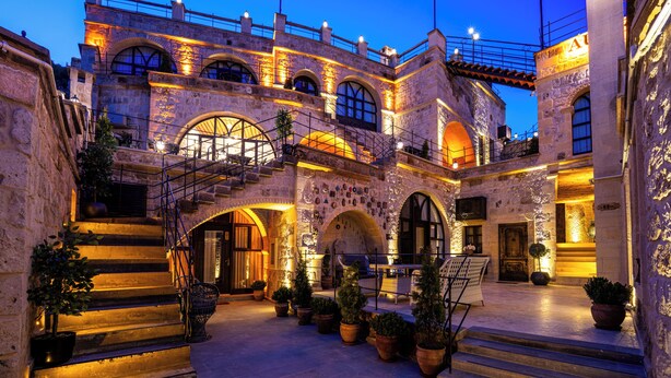 A historic stone building with multiple arches, a staircase, and potted plants. - Aurelia Cave Cappadocia (Urgup)