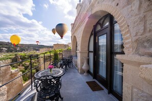 Un balcón con mobiliario exterior, un jarrón grande y vistas a un edificio histórico y globos aerostáticos.
