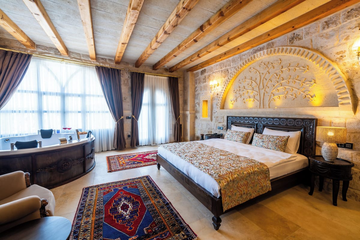 Quarto com uma cama grande, cabeceira curva, mesa de cabeceira, escrivaninha, cadeira, escrivaninha e janela com cortinas.
