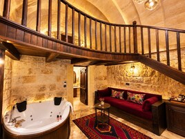 Un interior lujoso con pared de piedra, una bañera grande, un sofá rojo y una escalera de madera.
