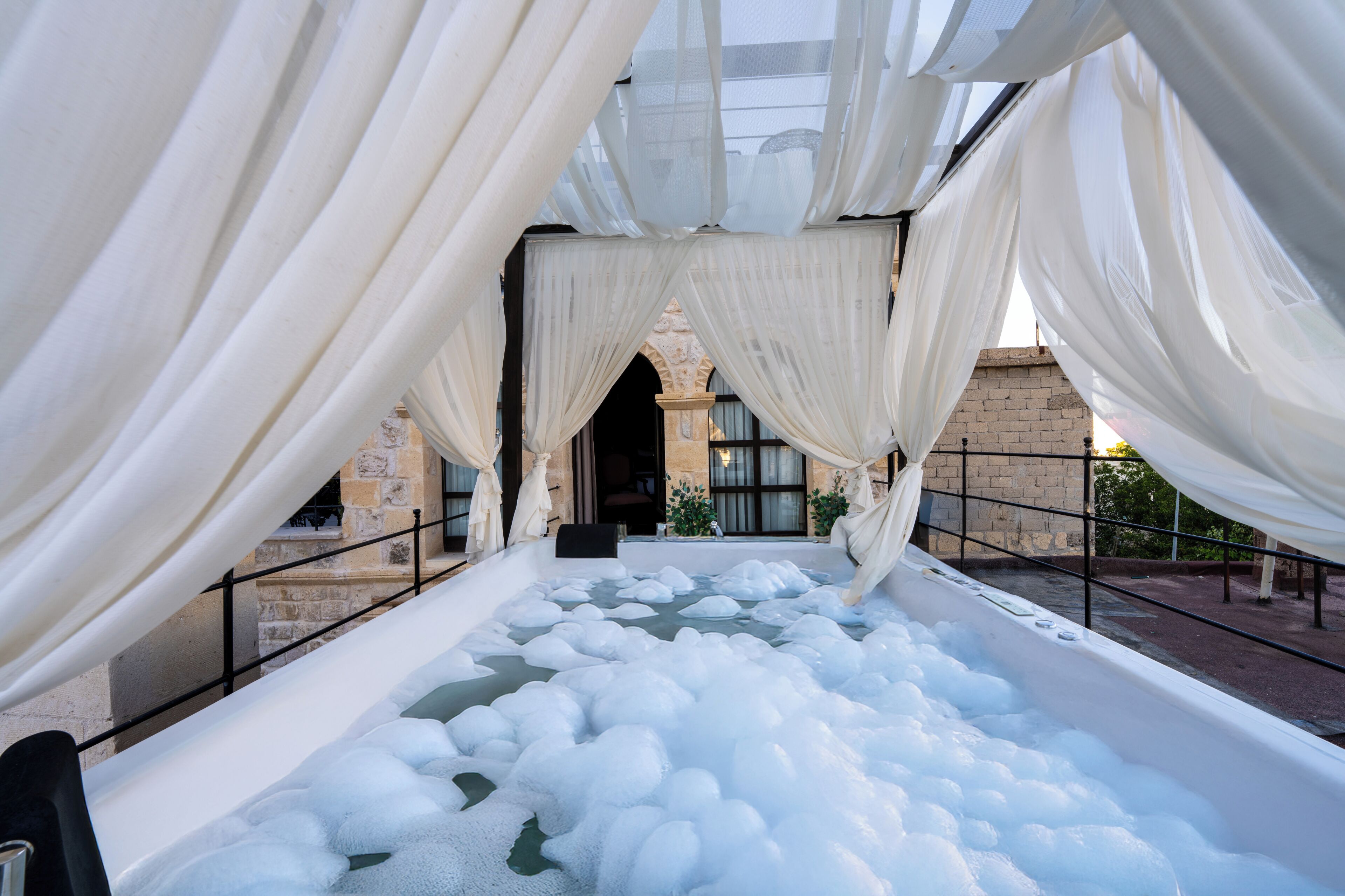 A spa area with a hot tub surrounded by white drapes and stone walls.