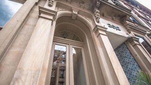 Una entrada de edificio con un amplio arco, una placa de número y un muro de piedra decorativo.