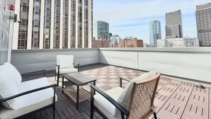 Una terraza en la azotea con zona de estar, vista del horizonte urbano y un rascacielos al fondo.