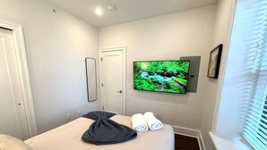 Una habitación de hotel con una cama, un televisor montado en la pared y una ventana con persianas.