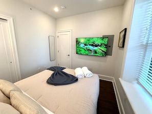 Ein Hotelzimmer mit Bett, Wandfernseher und Fenster mit Jalousien.