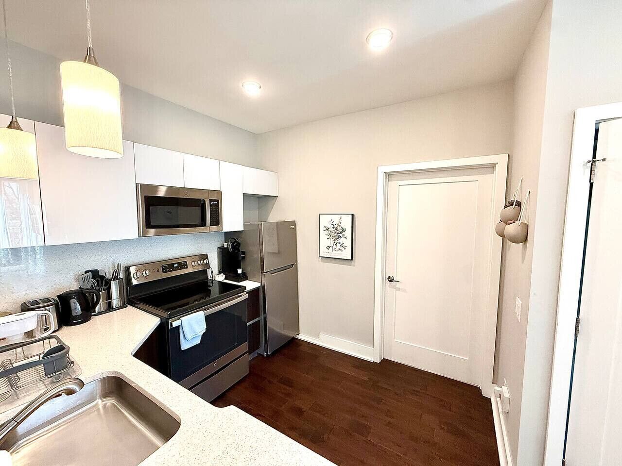 A modern kitchen with stainless steel appliances, a white countertop, and a wooden floor.