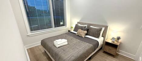 A bedroom with a bed, bedside table, lamp, and window.