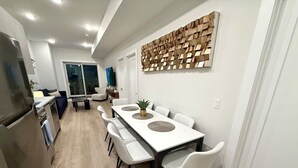 A modern kitchen with a dining area, white walls, and a wooden wall art piece. - Spacious Center City 2BR 2Bath Apt. with Balcony (Philadelphia)