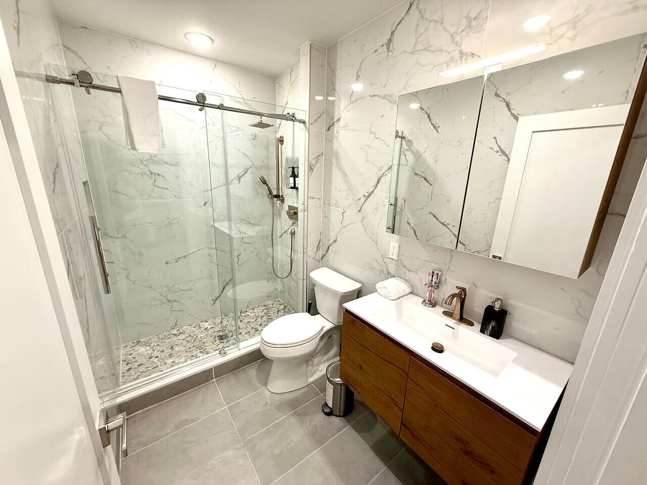 Un baño moderno con ducha de vidrio, inodoro y tocador con espejo.