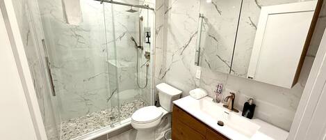 Un baño moderno con ducha de vidrio, inodoro y tocador con espejo.