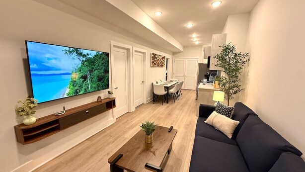 A modern living room with a flat-screen TV, a dark sofa, a wooden coffee table, and a dining area in the background. - Spacious Center City 2BR 2Bath Apt. with Balcony (Philadelphia)