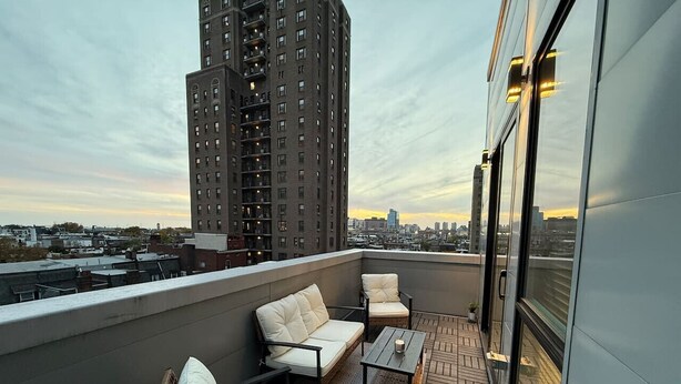 A rooftop terrace with a sofa, chairs, and a table, overlooking a cityscape. - Private Balcony | Gorgeous Center City Bilevel Apt (Philadelphia)