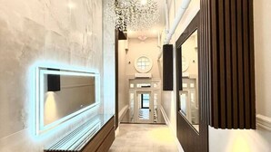 Un couloir moderne agrémenté d’un banc, d’un téléviseur fixé au mur et d’un lustre décoratif.