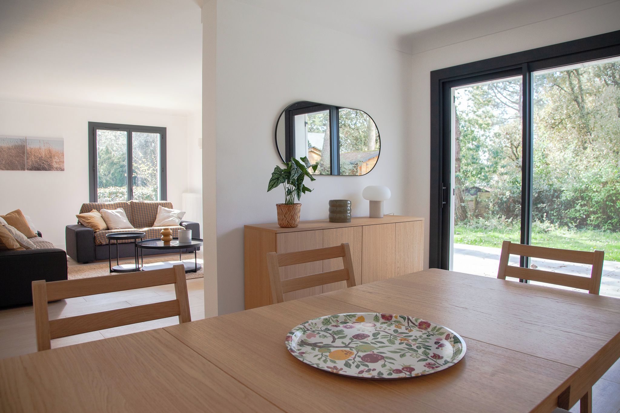 Un salon moderne avec un canapé, une table à manger et des chaises, une plante en pot et un miroir au mur.