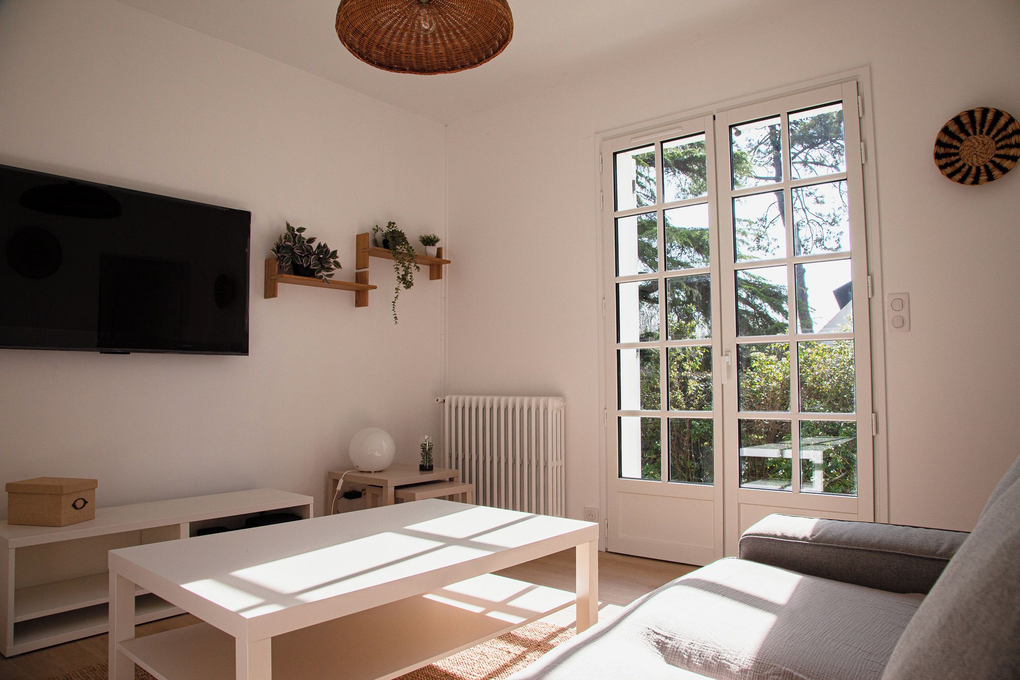 A living room with a television, a radiator, a window with a view of greenery, and a sofa.