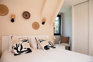 A bedroom with a bed, two wall-mounted lamps, and a window with a view.