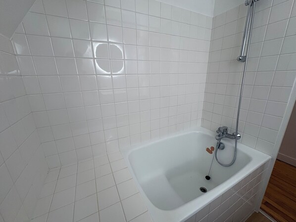 A bathroom with white tiled walls, a white bathtub, and a showerhead.