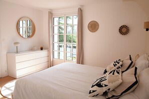 Een slaapkamer met een bed, een dressoir, een spiegel en een raam met gordijnen.