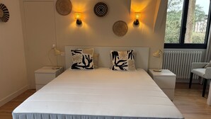 A modern bedroom with a large bed, two bedside tables, wall sconces, and a view of the outdoors. - Premium villa, enclosed garden, games room. (La Baule-Escoublac)