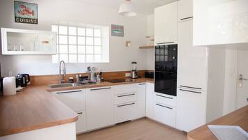 A modern kitchen with white cabinets, a black refrigerator, and a window with blinds.