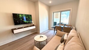 Un salon moderne doté d’un téléviseur à écran plat, d’un canapé, d’une table basse et d’un coin repas avec des chaises.