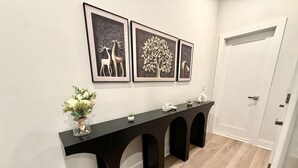 Un couloir avec une console noire, des œuvres d’art encadrées et une porte blanche.