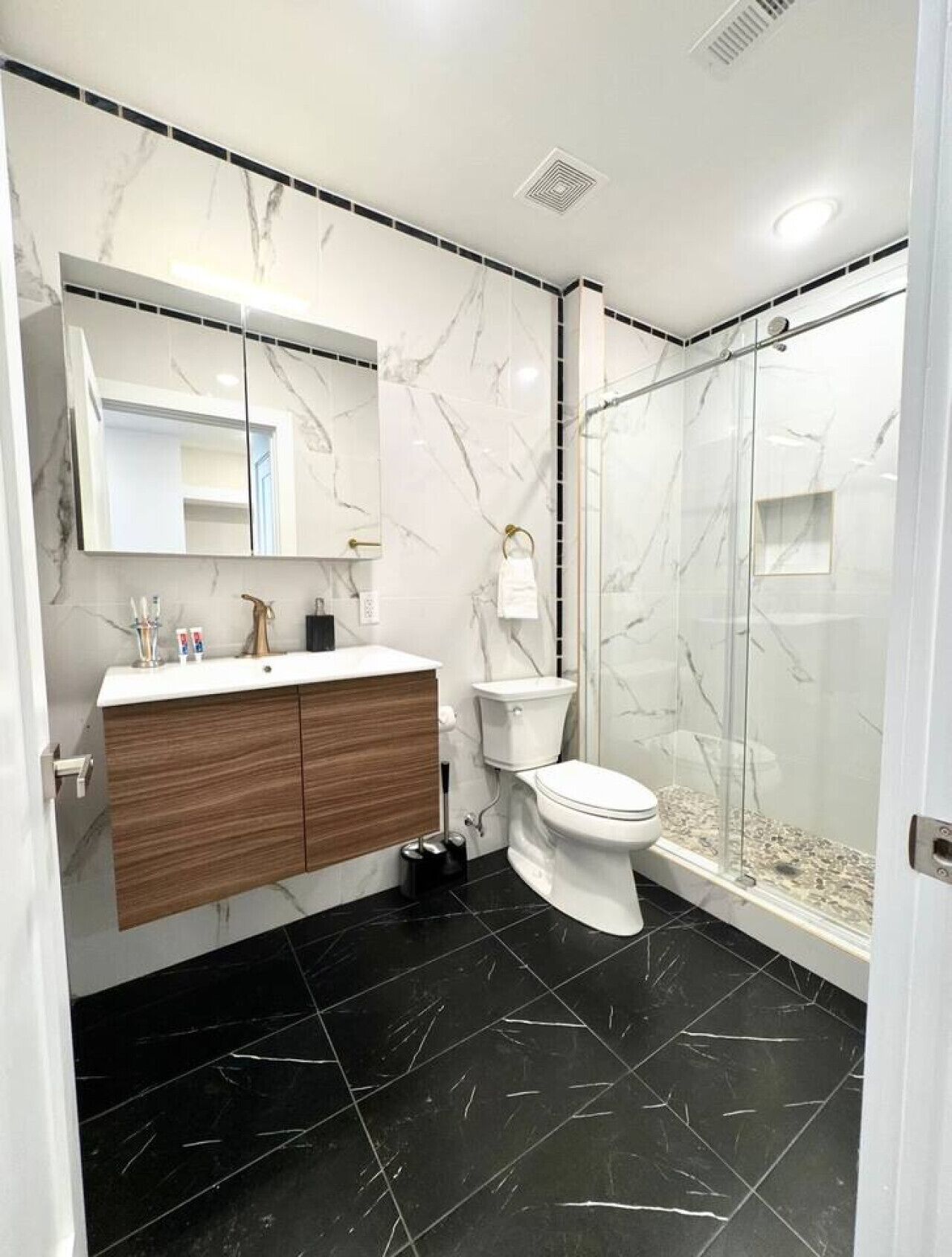 A modern bathroom with a marble vanity, a toilet, and a glass-enclosed shower.
