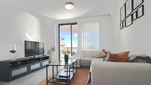 A modern living room with a flat-screen TV, a sofa, a coffee table, and a sliding glass door leading to a balcony. - Marinsa Gaviota (Torrox)