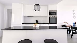A modern kitchen with a black countertop island, white cabinetry, and a hanging light fixture. - Marinsa Gaviota (Torrox)