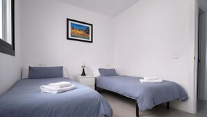 A bedroom with two beds, a nightstand with a lamp, a framed picture on the wall, and a door to the right. - Marinsa Gaviota (Torrox)