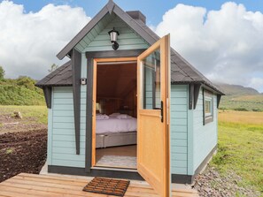 A small, light blue cabin with a wooden door open, revealing a bed and a window. - Little Luxe Lodges 2 (Kyle)