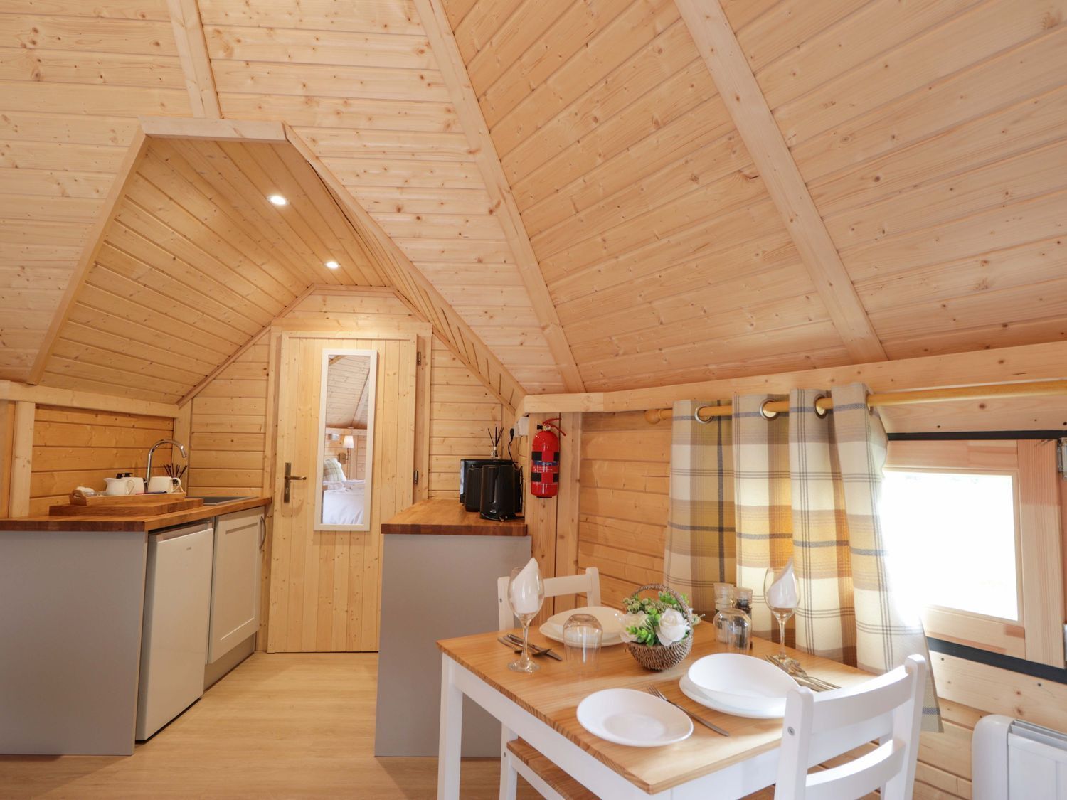 A wooden interior with a dining area, kitchenette, and a visible bedroom door.