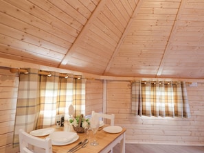 A wooden cabin interior with a dining table set for four, two chairs, and a window with plaid curtains. - Little Luxe Lodges 2 (Kyle)
