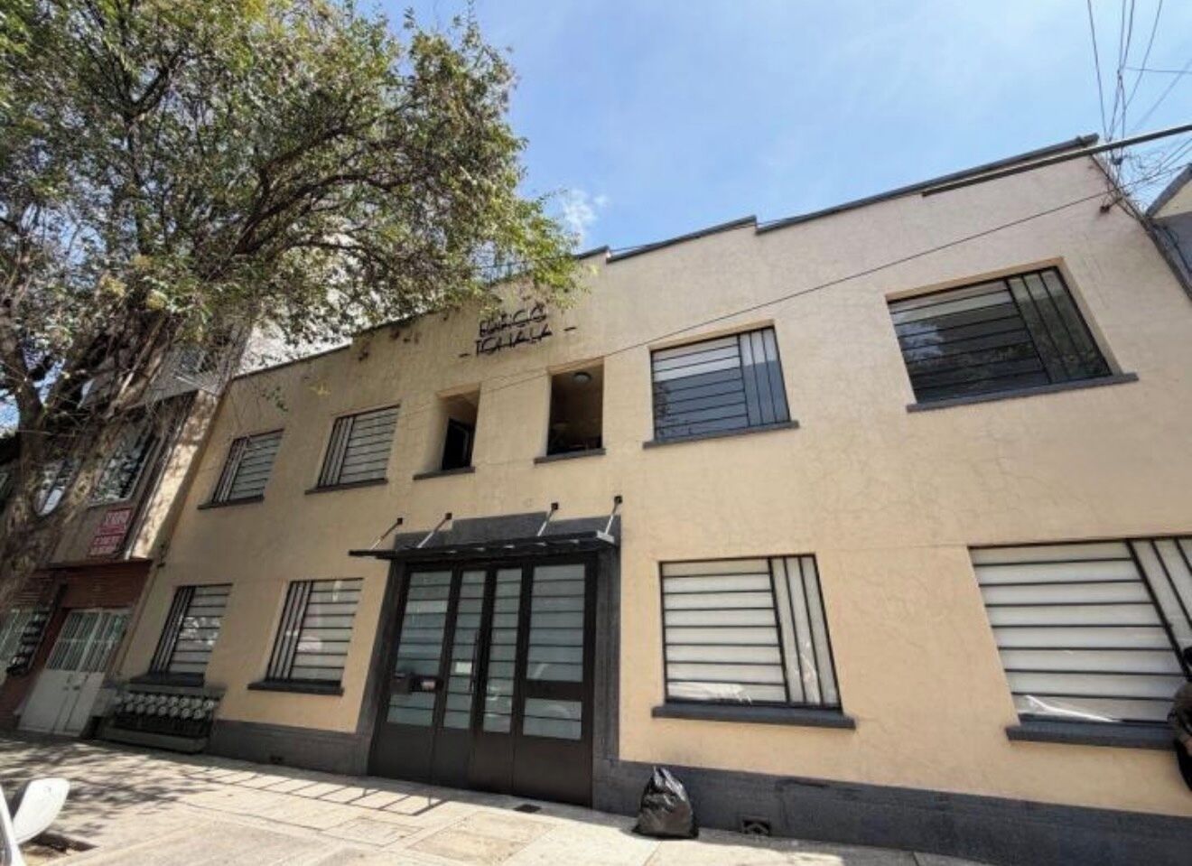 Un bâtiment à la façade beige, doté de nombreuses fenêtres et d’une entrée centrale avec une porte.