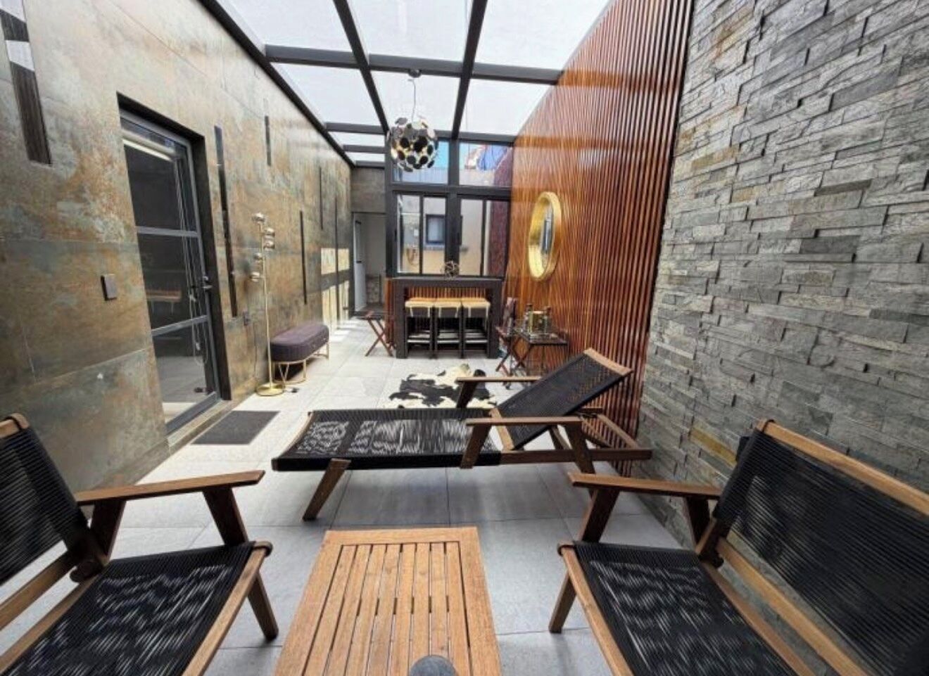 A modern outdoor seating area with wooden furniture and a stone wall.