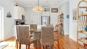 A modern kitchen with white cabinets, a stainless steel refrigerator, wicker chairs, and a hanging light fixture. - Rhapsody in Blues (Port St. Joe)