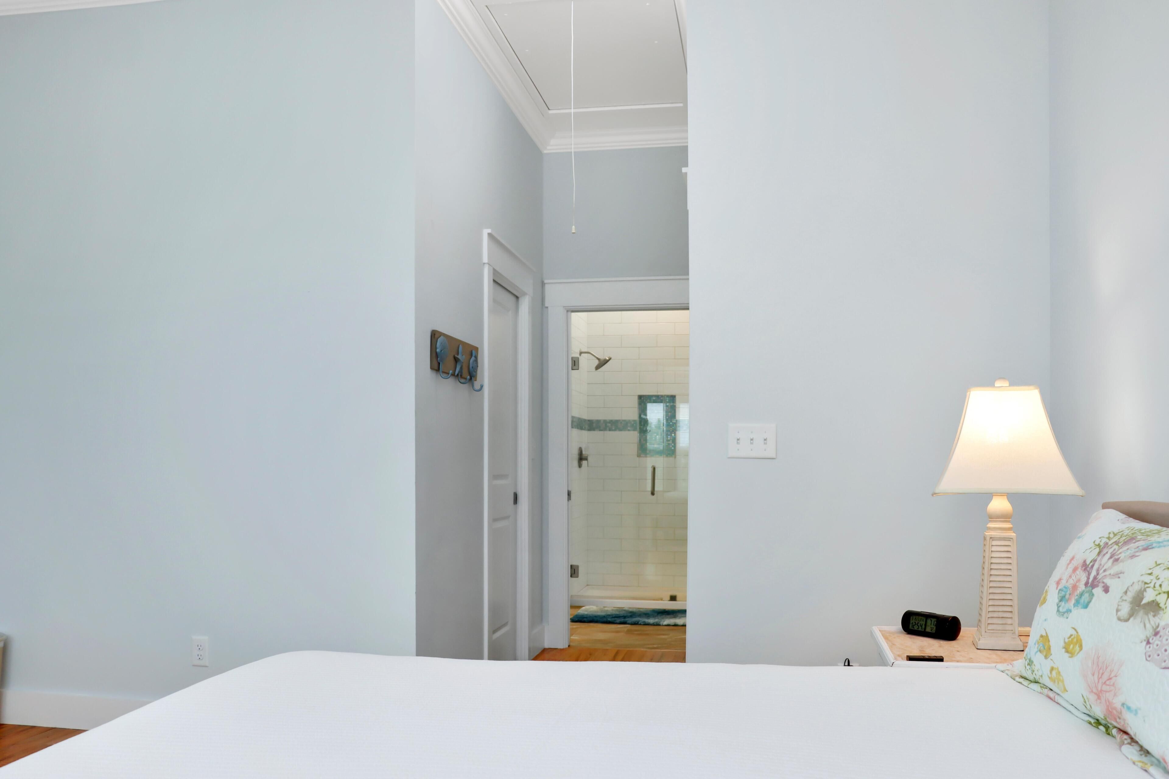 A hotel room with a bed, a nightstand with a lamp, a digital clock, and a view into the bathroom.