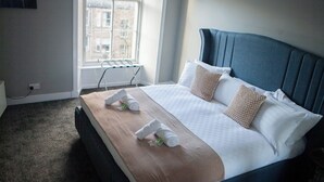 A hotel room with a bed, a window, a wall-mounted towel rack, and a view of buildings outside. - The West Nest For Six - Pass the Keys (Glasgow)