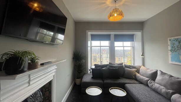 A living room with a fireplace, a sofa, a TV, and a window with blinds. - The West Nest For Six - Pass the Keys (Glasgow)