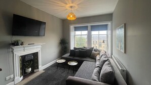 A living room with a fireplace, a sofa, a television, and a large window. - The West Nest For Six - Pass the Keys (Glasgow)