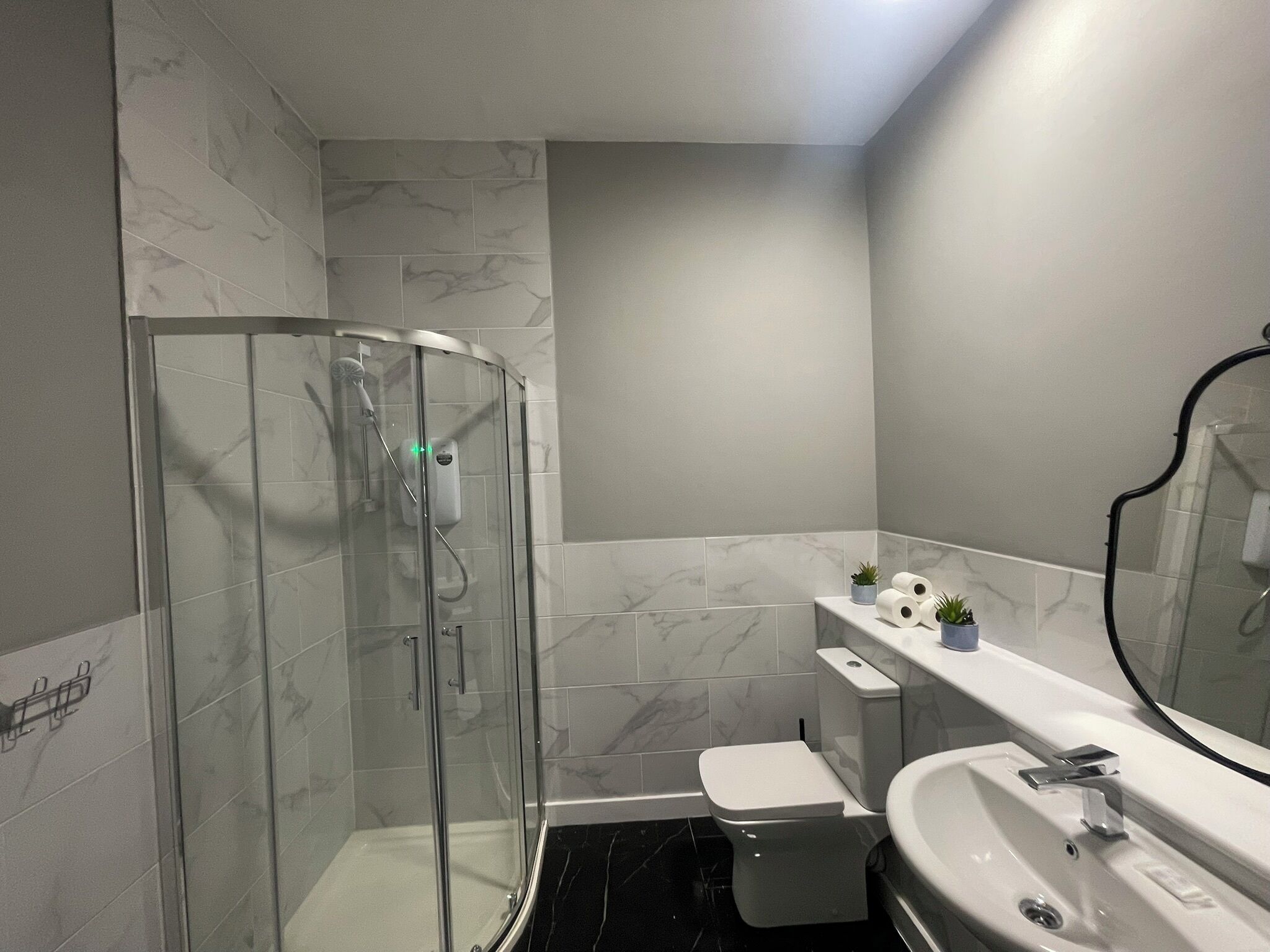 A bathroom with a glass-enclosed shower, a toilet, a sink with a mirror, and a marble-tiled wall.
