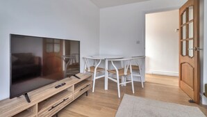 Ein modernes Wohnzimmer mit Flachbildfernseher, Holzunterhaltungseinheit, weißem runden Tisch und passenden Stühlen.