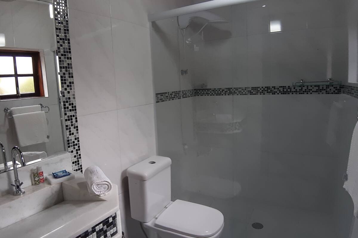Un bany amb dutxa de vidre, un lavabo blanc, un mirall i una finestra.