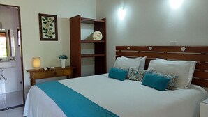 Quarto com teto de madeira, cama com roupa de cama branca e azul-turquesa, mesa de cabeceira, luminária fixada na parede e guarda-roupa de madeira.