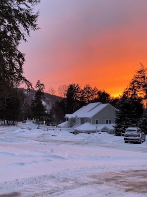 A residential area with houses, a car, and a snowy landscape during sunset. - Ski's The Day: Winsome 3-bedroom mountain townhome with AC in Jiminy Peak (Hancock)