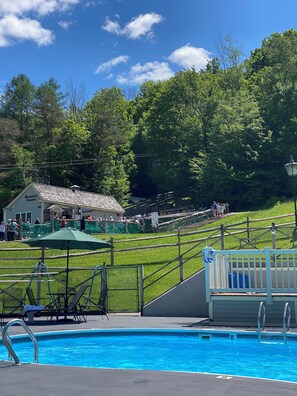 A swimming pool with a green umbrella, a small building labeled 'Mountain Coaster,' and a fenced area with people. - Ski's The Day: Winsome 3-bedroom mountain townhome with AC in Jiminy Peak (Hancock)
