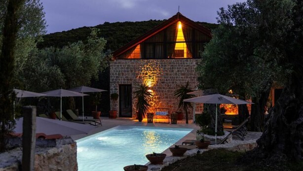 Un bâtiment en pierre avec une piscine, entouré de parasols et de chaises longues.